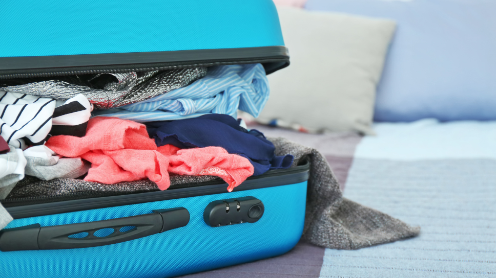 Open blue suitcase stuffed with clothes on a bed