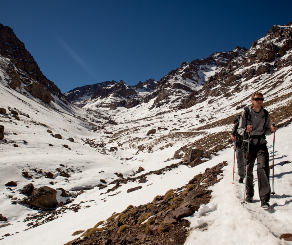 Hikers with trekking poles on a snowy mountain trail in a rocky valley