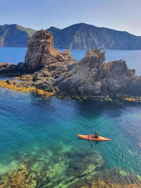 Kayaker paddling in clear turquoise water beside jagged rocks on the Skikda coast