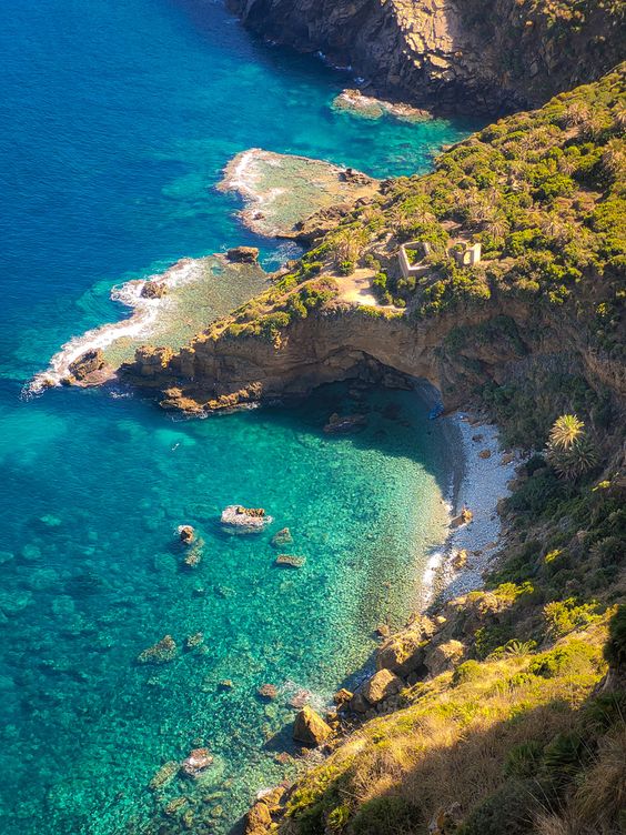 Turquoise cove with a rock arch and green hillside on the Annaba coast