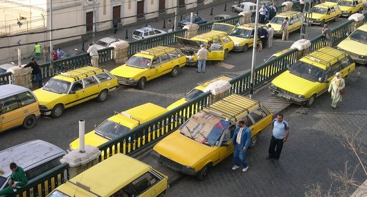 Crowd of yellow taxis waiting in a busy taxi lot with drivers standing nearby