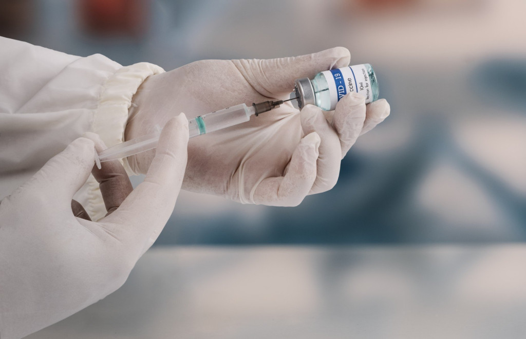 Gloved hands drawing a vaccine dose from a vial into a syringe