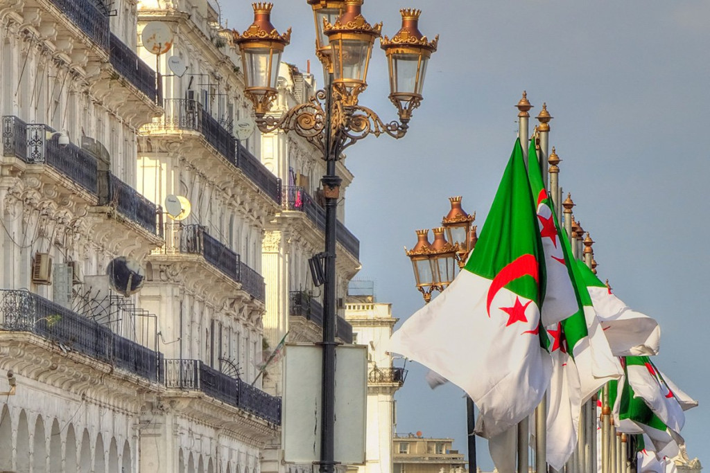 Algerian flags and ornate street lamps in front of white colonial buildings in Algiers