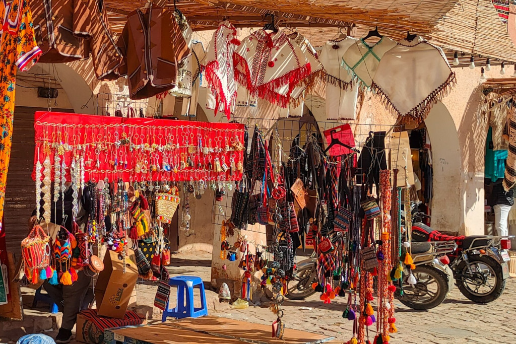 Market stall with hanging bags, ponchos and tassels beside parked scooters