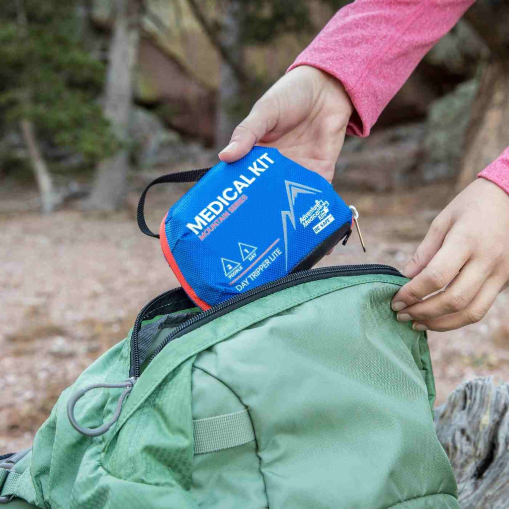 Hiker packing a small blue first aid kit into a green daypack