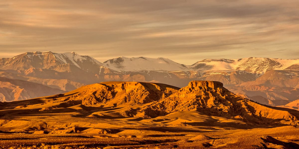 Snow-capped mountains above golden desert hills at sunset