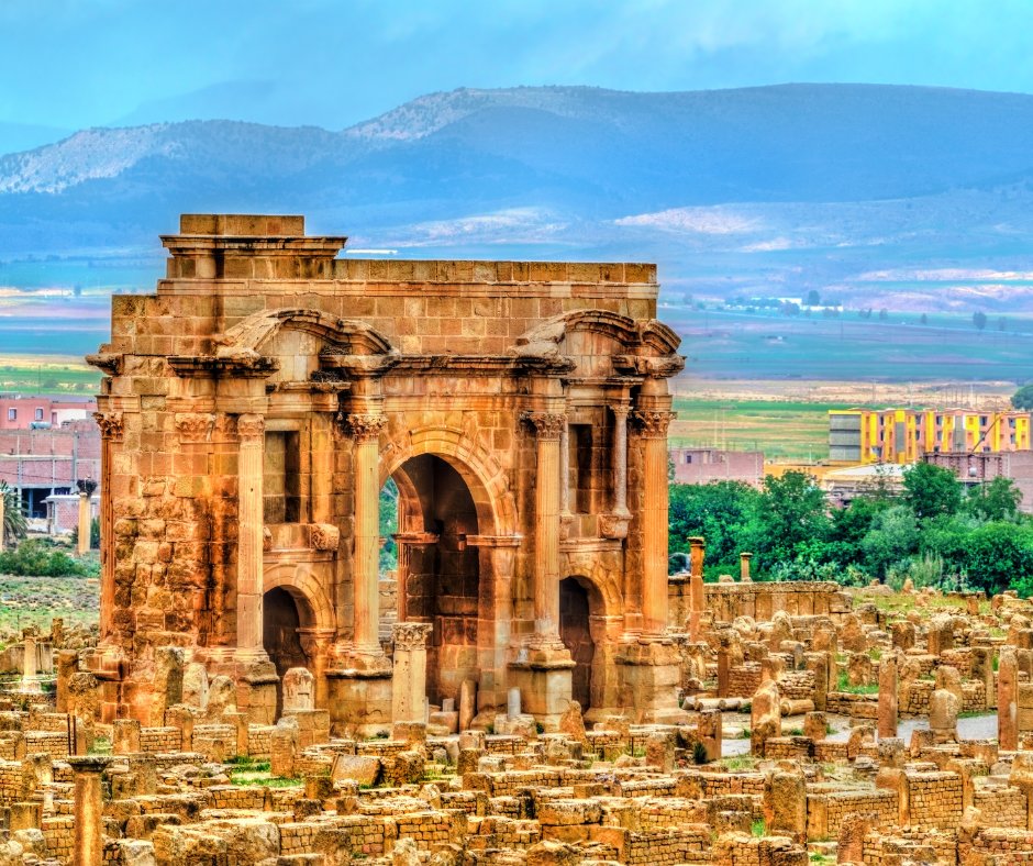 Trajan's Arch at Timgad in warm sandstone with ruins and hills behind