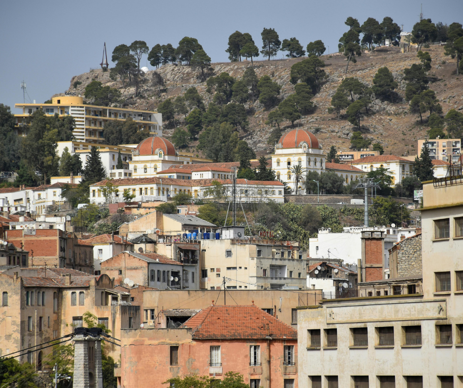 Hillside neighborhood with red tiled roofs and a domed building behind a wooded slope