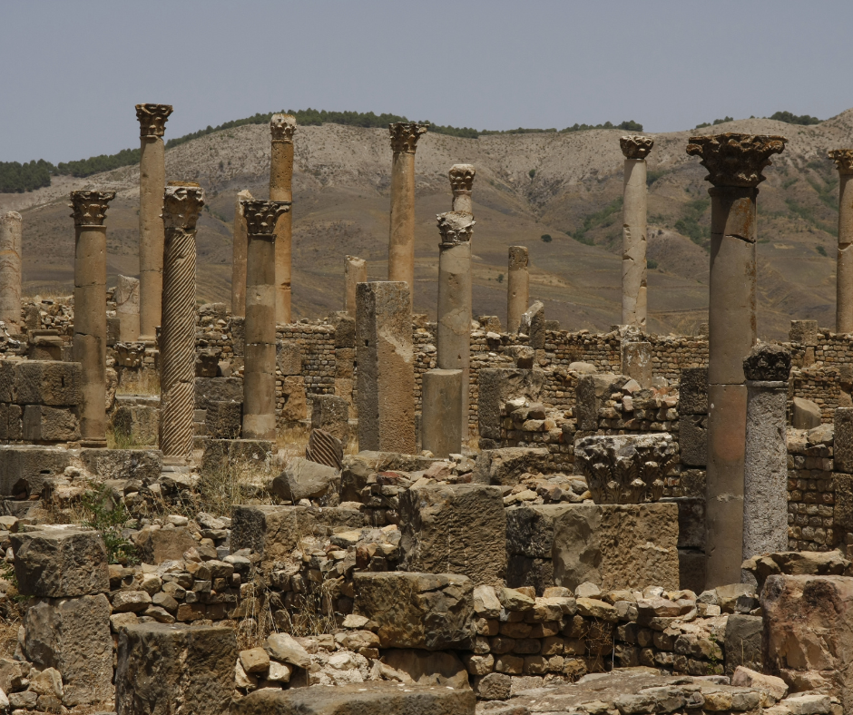 Weathered Corinthian columns among Roman ruins at Djemila with hills behind