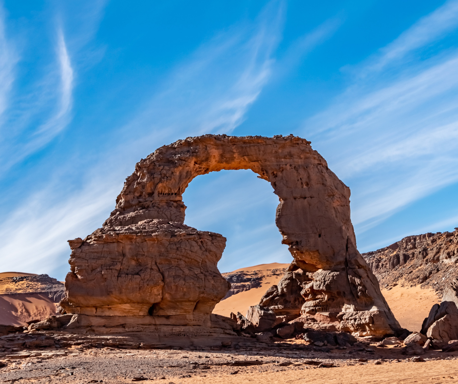 Natural sandstone arch rising from orange sand in the Tadrart Rouge, Djanet