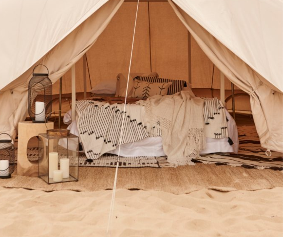 Canvas bell tent with a bed, striped blankets and candle lanterns on desert sand