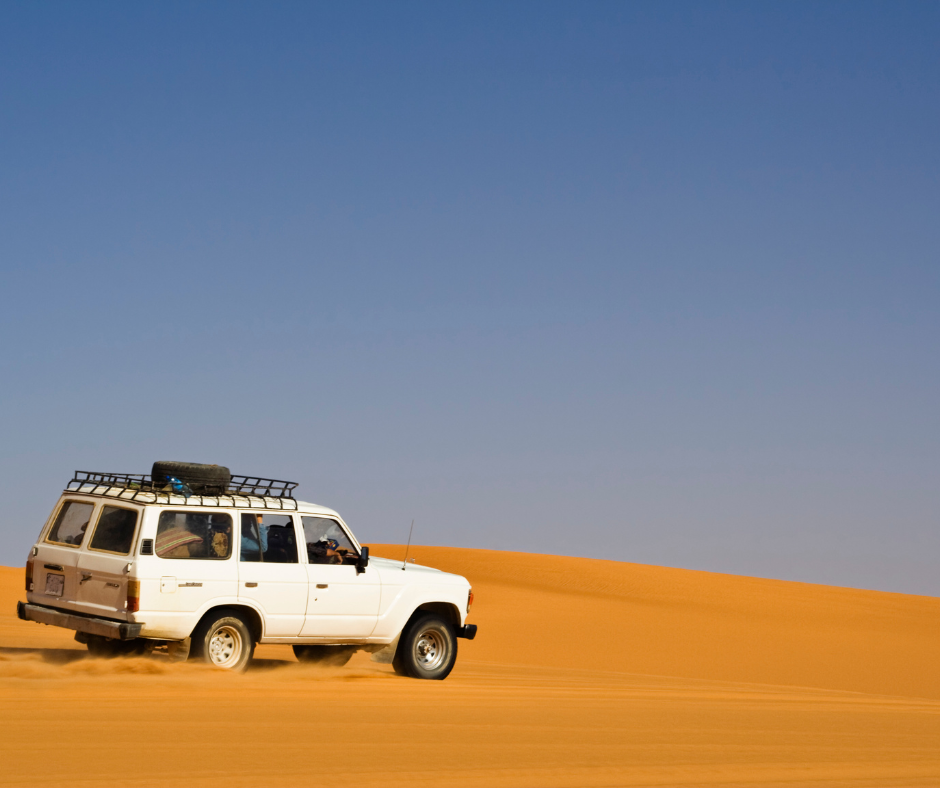 White 4x4 driving up a sand dune in the Sahara
