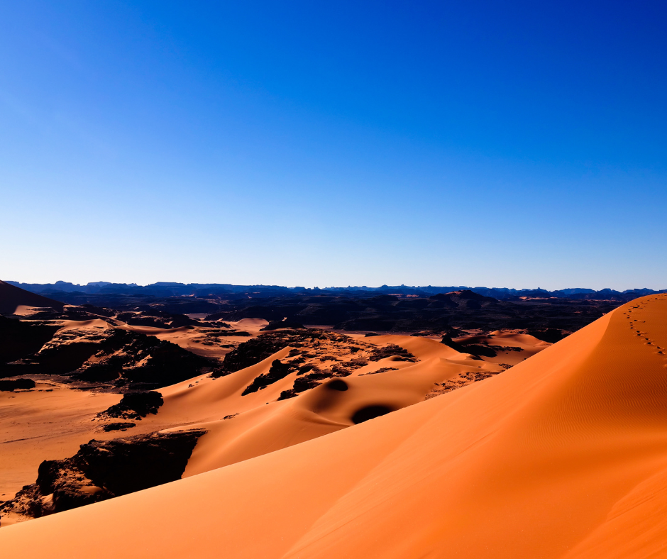 Orange dunes and dark rock outcrops of the Tassili n'Ajjer under a deep blue sky