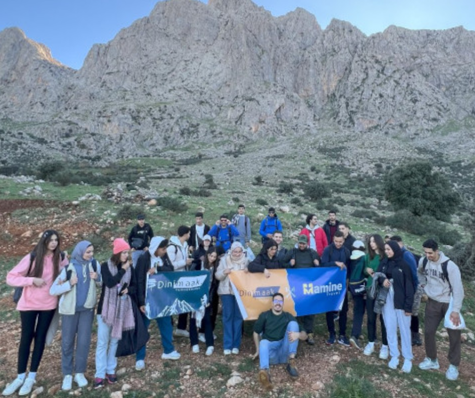 Group of young hikers holding sponsor banners below a rocky Djurdjura ridge
