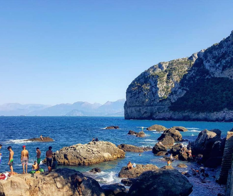 Swimmers on rocks beside deep blue water at Les Aiguades near Béjaïa