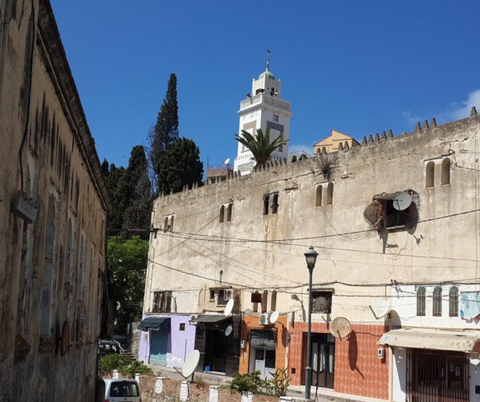 Old town street in Béjaïa with a weathered wall and a white minaret