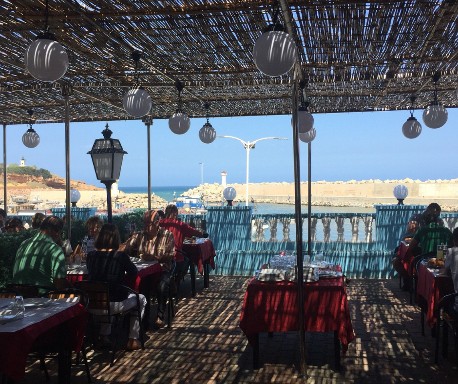 Harbor-side restaurant terrace at Tipaza with red tablecloths and a view of the port