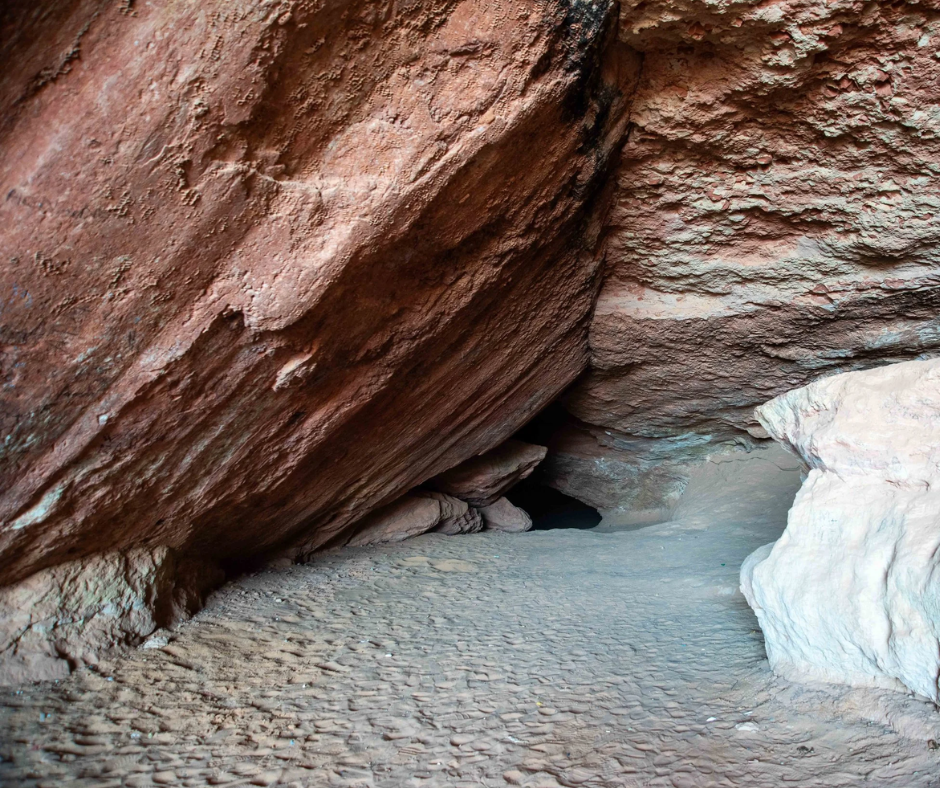 Cave opening under red sandstone with a sandy floor