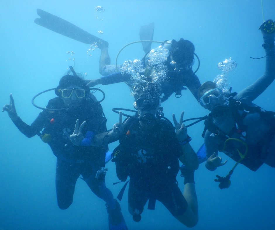 Three scuba divers posing underwater with peace signs in blue water