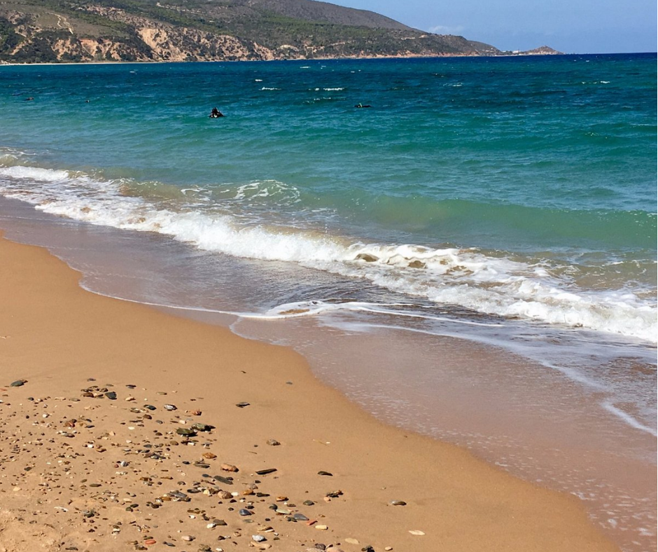 Sandy beach with small waves and a rocky headland at Les Andalouses